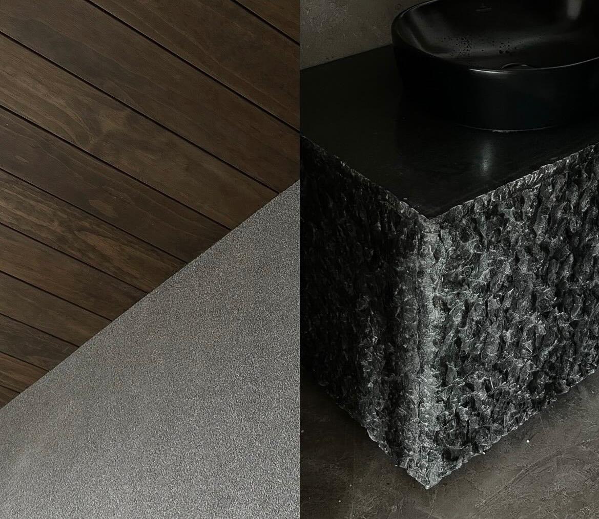 Dark-stained timber ceiling meeting a sandblasted stone wall, beside a rough-cut black stone vanity with a matte black basin