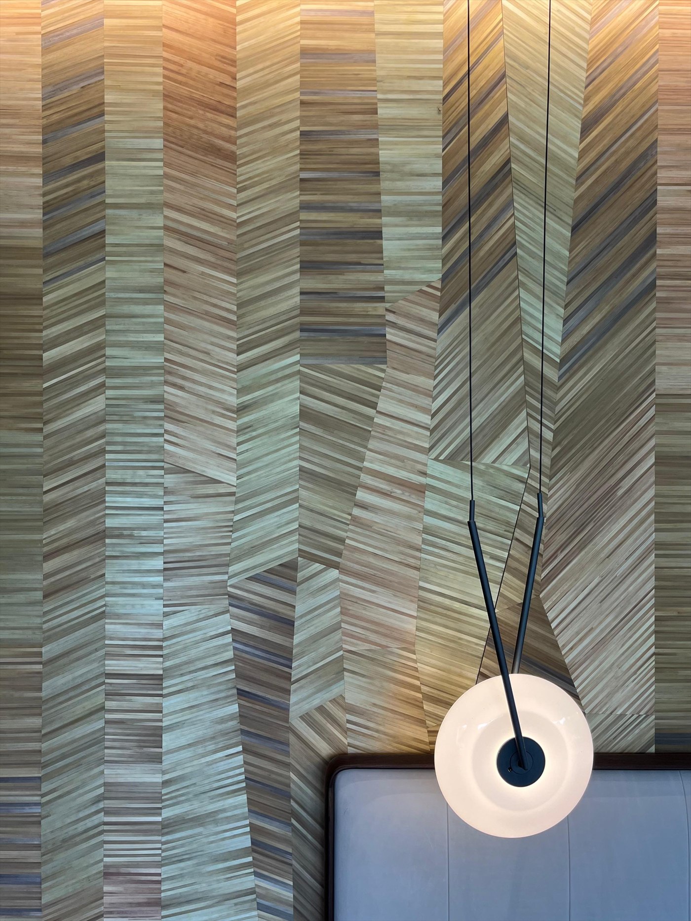 Faceted straw-marquetry headboard wall with a suspended white disc pendant light
