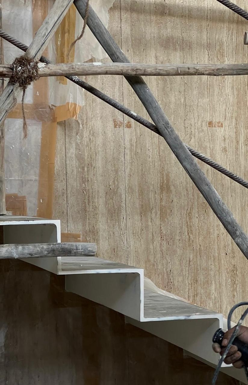Folded-plate steel staircase being installed against the travertine wall, still braced with timber props