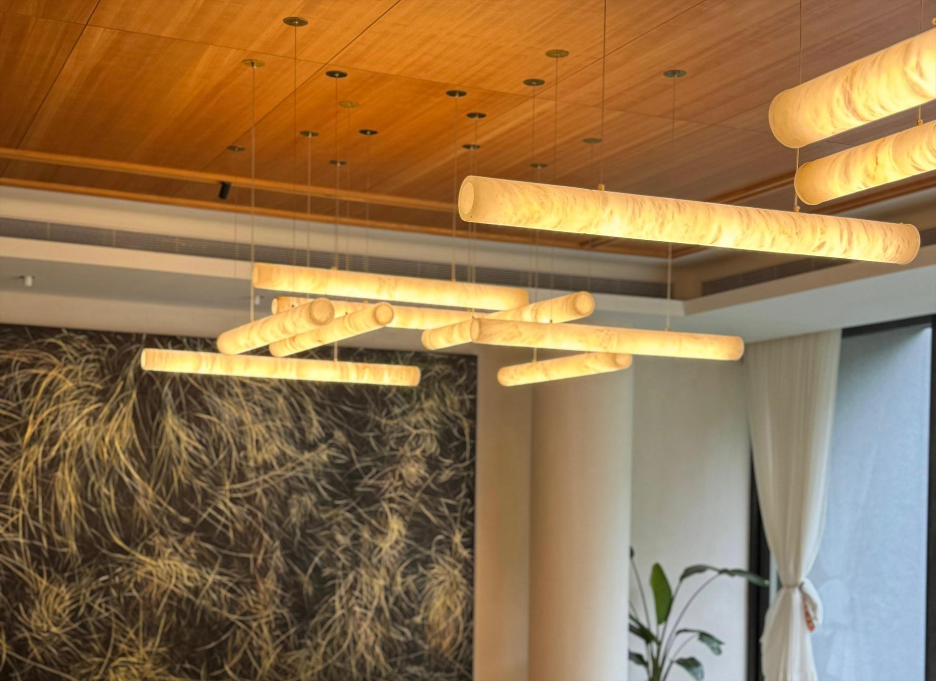 Cluster of alabaster tube pendants beneath a warm timber ceiling, in front of a large abstract artwork