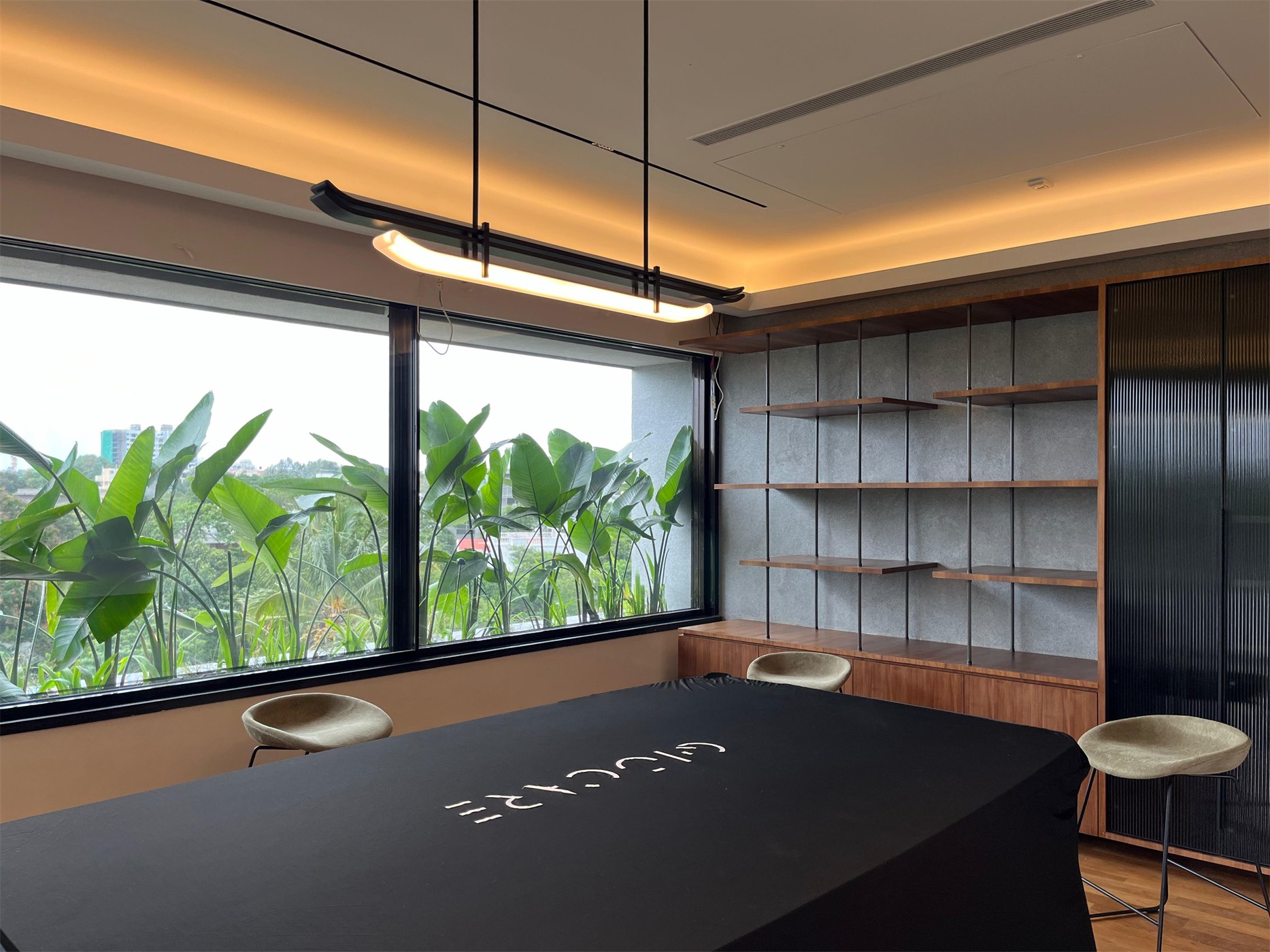 Games room at The Stepped Haven with a covered table, suspended linear light and a window full of banana plants