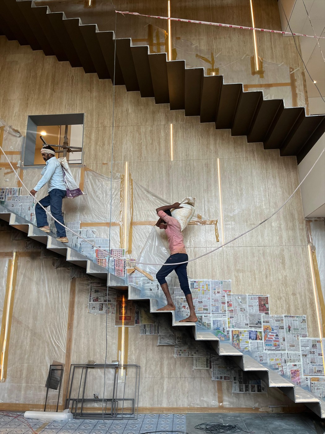 Workers carrying material up the folded-plate staircase in front of the stone-clad feature wall